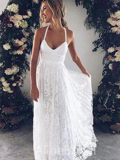 a woman wearing a white dress standing in front of a floral arch with her hand on her hip