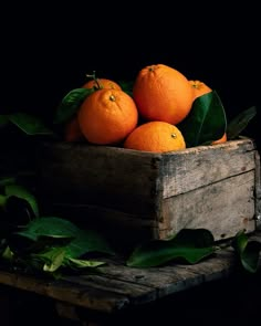 a wooden crate filled with oranges sitting on top of green leaves next to a black background