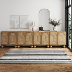 a room with a rug, mirror and vases on the sideboard in it