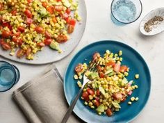 two plates with corn and tomatoes on them next to a measuring spoon, salt and pepper shakers