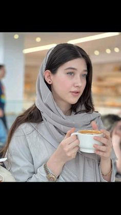 a woman holding a cup of coffee and looking at the camera while wearing a scarf