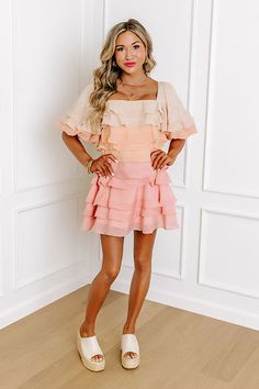 a woman standing in front of a white wall with her hands on her hips and legs crossed