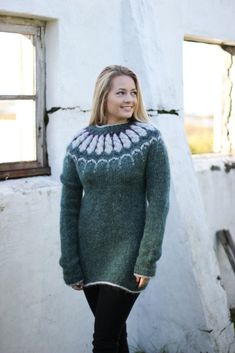 a woman standing in front of a white building wearing a green sweater and black pants