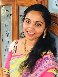 a woman in a yellow and pink sari smiles at the camera while sitting on a chair