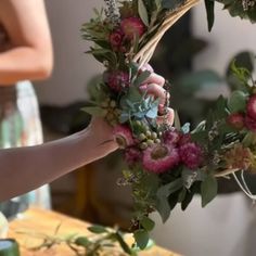 a woman is making a wreath with flowers and succulents