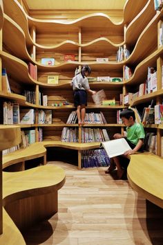 two children reading books in a library with shelves full of books and wooden benches on the floor