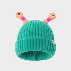 a green knitted hat with two orange eyes on the front and one pink ear