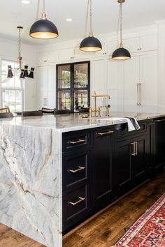 a large kitchen with marble counter tops and black cabinets, along with two pendant lights hanging from the ceiling