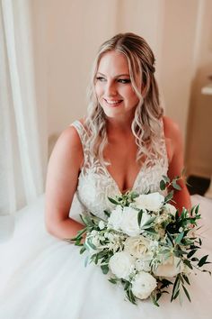 a woman in a wedding dress sitting on a bed holding a bouquet of white flowers