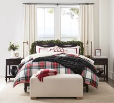 a bed with plaid comforter and pillows in front of a large window on a rug