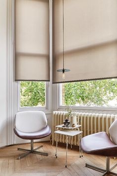 two chairs and a table in front of a window with roller shades on the windowsill