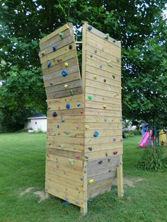 an outdoor climbing wall made out of wooden planks in the grass with trees behind it