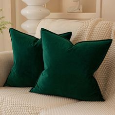 two green pillows sitting on top of a couch next to a white vase and lamp