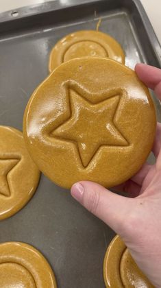 a person holding a cookie in front of some cookies on a baking sheet with icing