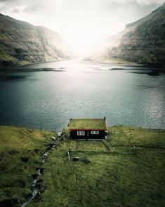 an aerial view of a small house in the middle of a lake with mountains behind it