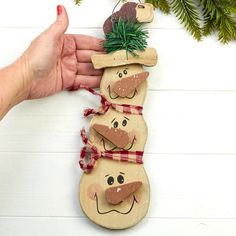 a hand holding a wooden snowman ornament on top of a white table