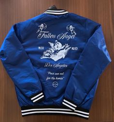 Our Fallen Angel Summer collection is finally available now! Don't miss out! Were super proud of this one! This dope limited edition series commemorates five years we've lost our dear homie. Our first piece is our Super fly royal blue Varsity Jacket, this one goes too hard. Front is embroidered AXEL with a Sanskrit inspired calligraphy bykineks. The font embeds the 5 years out detail. The back is a beautiful heat pressed process with our fallen angel, pour one out for the homie graphic design. Very limited selection of Medium, Large and XL Available now. 100% proceeds go to our Axel Lives Scholarships supporting out of the box, rebel multidisciplinary artists and designers in need. Blue Outerwear With Embroidered Logo For College, Blue Embroidered Outerwear For College, Navy Letter Print Streetwear Outerwear, Navy Letter Print Outerwear For Streetwear, Retro Blue Outerwear With Letter Print, Urban Blue Outerwear With Graphic Print, Retro Blue Outerwear With Graphic Print, Blue Graphic Print Outerwear For Streetwear, Blue Crew Neck Track Jacket For Streetwear