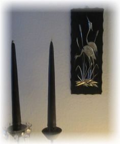 two black candles sitting next to each other in front of a painting on the wall