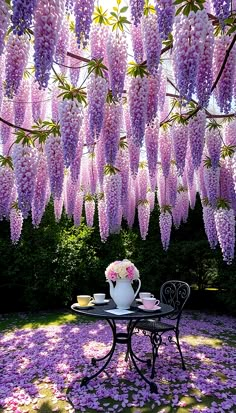 a table and chairs under purple flowers on the ground