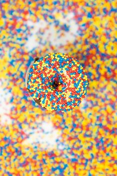 a sprinkle covered donut sitting on top of a colorful tablecloth with multicolored sprinkles