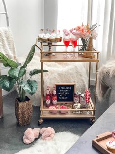 a bar cart filled with drinks and snacks on top of a table next to a potted plant