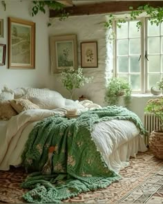 a bedroom with white walls and green blankets on the bedspread, potted plants in window sill