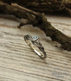 a silver ring sitting on top of a wooden table next to a twig branch