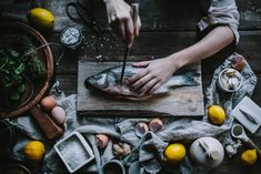 a person cutting up fish on top of a wooden table next to lemons and other food