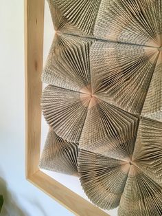 a close up of a wall hanging made out of folded paper and wood sticks with a plant in the background