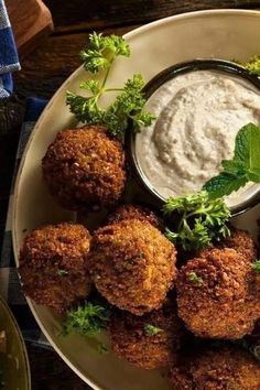 a white plate topped with falafel next to a bowl of ranch dressing