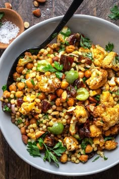 a bowl filled with corn and vegetables on top of a wooden table next to two spoons