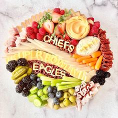 a platter filled with cheeses, fruits and vegetables on top of a marble counter