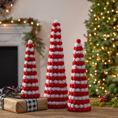 three red and white christmas trees sitting on top of a table next to a fireplace