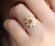 a woman's hand wearing a gold ring with an orange flower on the middle