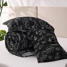 a black and white floral comforter on a bed next to a potted plant