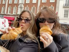 two women are eating croissants in front of a car on the street