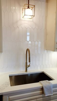 a kitchen sink under a hanging light in a white tile backsplash with hexagonal tiles on the wall