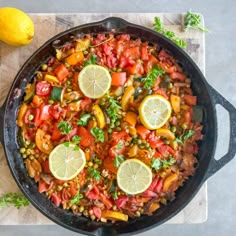 a skillet filled with vegetables and lemons on top of a cutting board