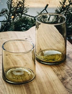 two glasses sitting on top of a wooden table next to christmas tree branches in the background