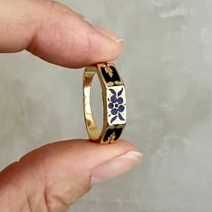 This antique Victorian memory ring is a finely crafted piece, designed in 18-karat gold and adorned with intricate black enamel. The enamel is decorated with a delicate floral design, featuring a "forget-me-not" flower motif. This flower, often associated with remembrance and enduring love, was a popular symbol in Victorian jewelry, adding sentimental and symbolic value to the piece. The outer band of the ring is richly decorated with black enamel, which provides a striking contrast to the warm glow of the gold. The centerpiece of the design is the forget-me-not flower, beautifully rendered in enamel, with its delicate petals symbolizing love, remembrance, and fidelity. The floral design gives the ring a timeless elegance, making it not only a piece of jewelry but also a sentimental keepsa Edwardian Rings Antique, Wedding Ring Earthy, Vibtage Rings, Diamond Ring Not Engagement, Ancient Gold Jewelry, Enamel Engagement Ring, Vintage Gold Wedding Ring, Queer Engagement Rings, Colored Gemstone Engagement Rings