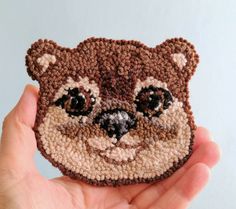 a hand holding up a small crocheted bear brooch with eyes and nose