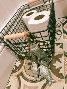 two metal fish figurines sitting on top of a tiled floor next to rolls of toilet paper