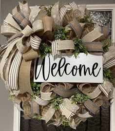 a welcome sign hanging on the front door of a house decorated with burlocks and wreaths