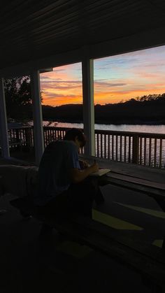 a person sitting on a bench in front of a body of water at sunset with the sun setting