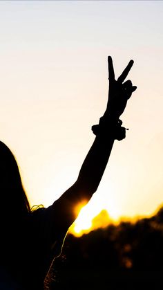 a person making the peace sign with their hands in front of an orange and blue sky