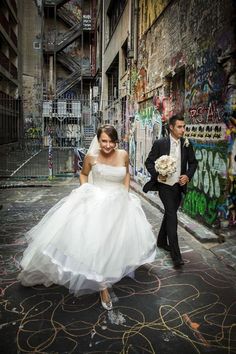 a bride and groom are walking down the street in front of graffiti covered buildings with their backs to each other