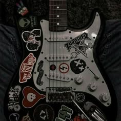 an electric guitar with many stickers on it's body and neck, sitting in someones lap