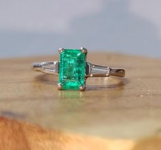 an emerald and diamond ring sitting on top of a wooden table