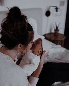 a woman holding a baby in her arms while sitting on a bed with white sheets