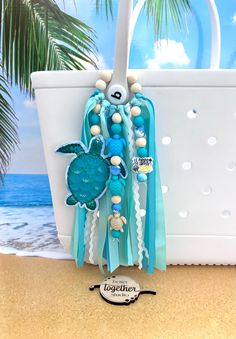 a blue sea turtle and shell beaded bracelet on a beach with the ocean in the background